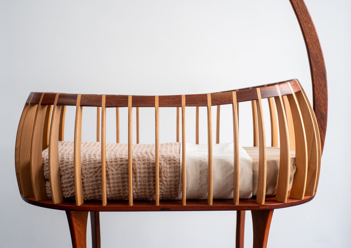 De mand van de handgemaakte wieg met beuken spijlen en mahonie rand, gedekt met wollen dekentje